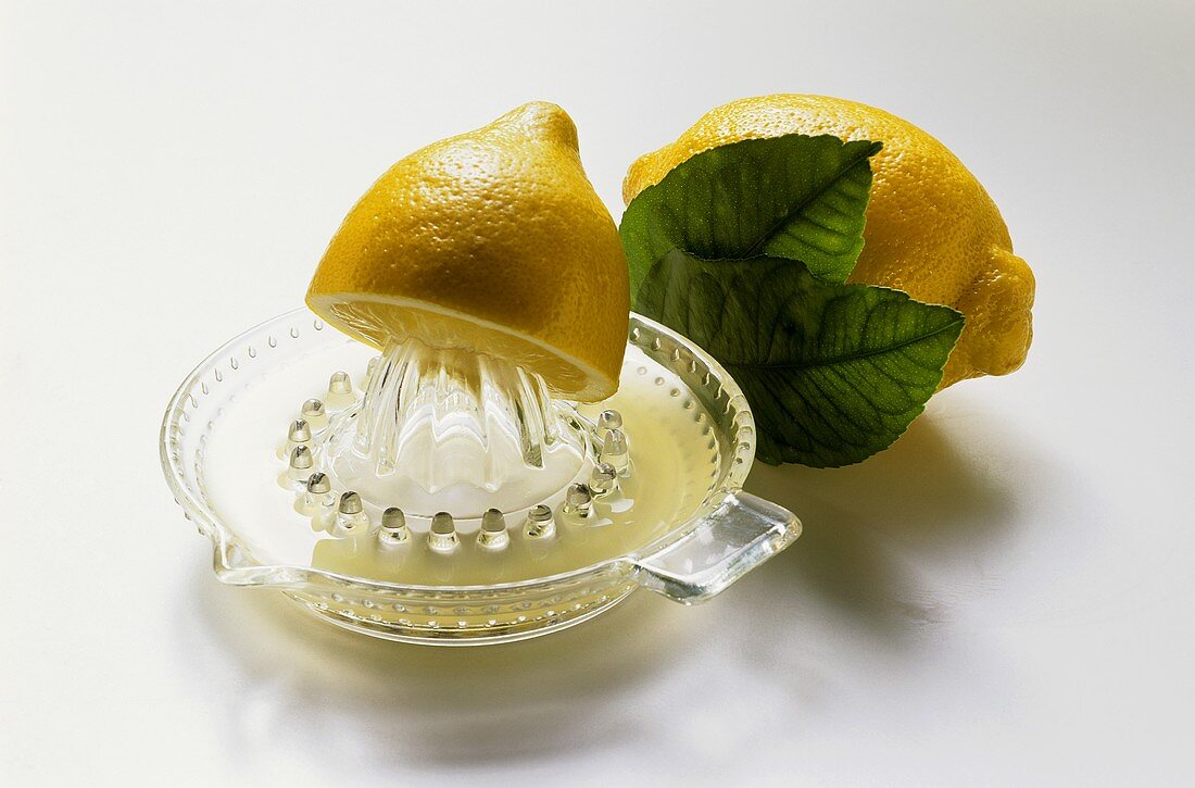 Eine Zitronenhälfte auf der Zitruspresse vor ganzer Zitrone