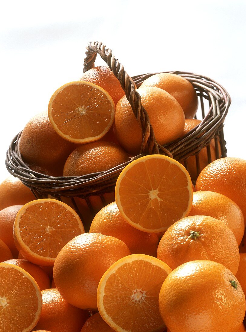 Orangen, ganz und halbiert, vor und in einem Korb