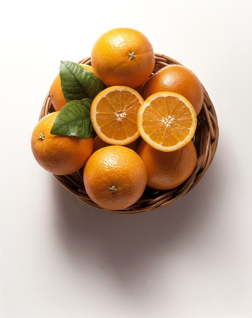 Whole oranges & two halves with leaves in basketwork bowl