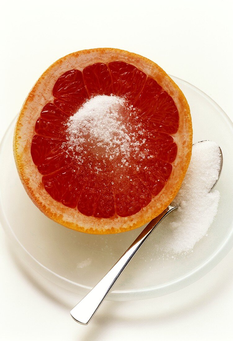 Pink grapefruit half with sugar on plate with spoon