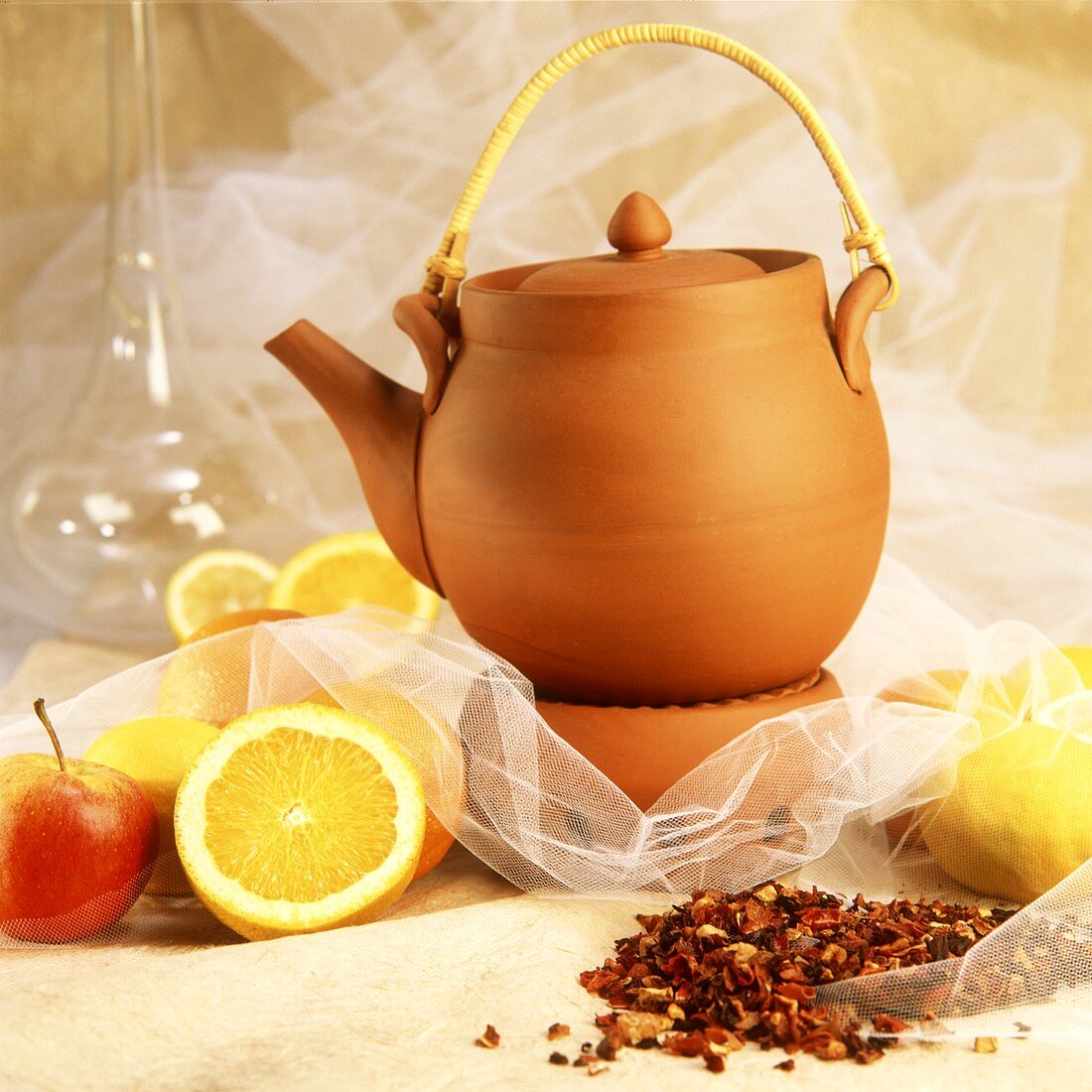 Teekanne aus Ton, daneben Früchtetee, Zitronen und Äpfel