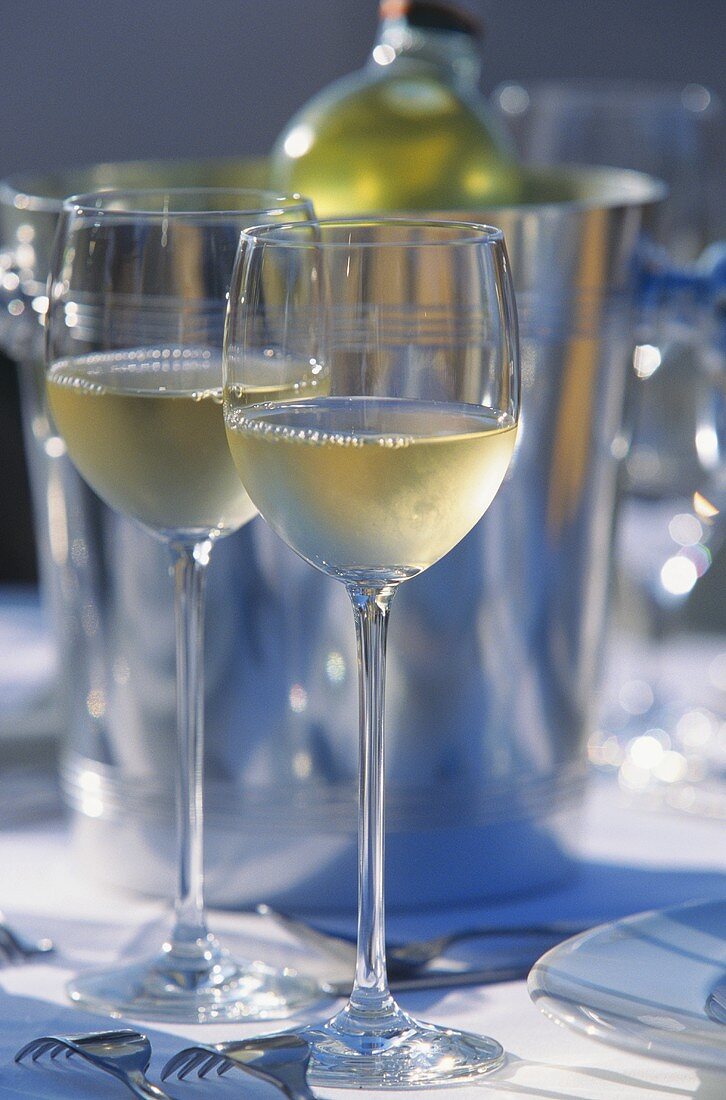 Two glasses of white wine on table in front of wine cooler