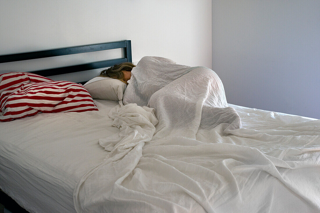 Schlafende Frau unter weißem Leinenbettzeug bei Tageslicht mit rot-weiß gestreiften Kissen auf der linken Seite