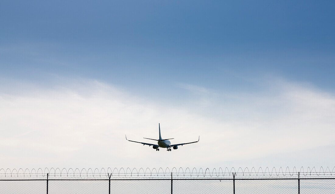 Rear view of Commercial Airplane flying over barbed wire fence