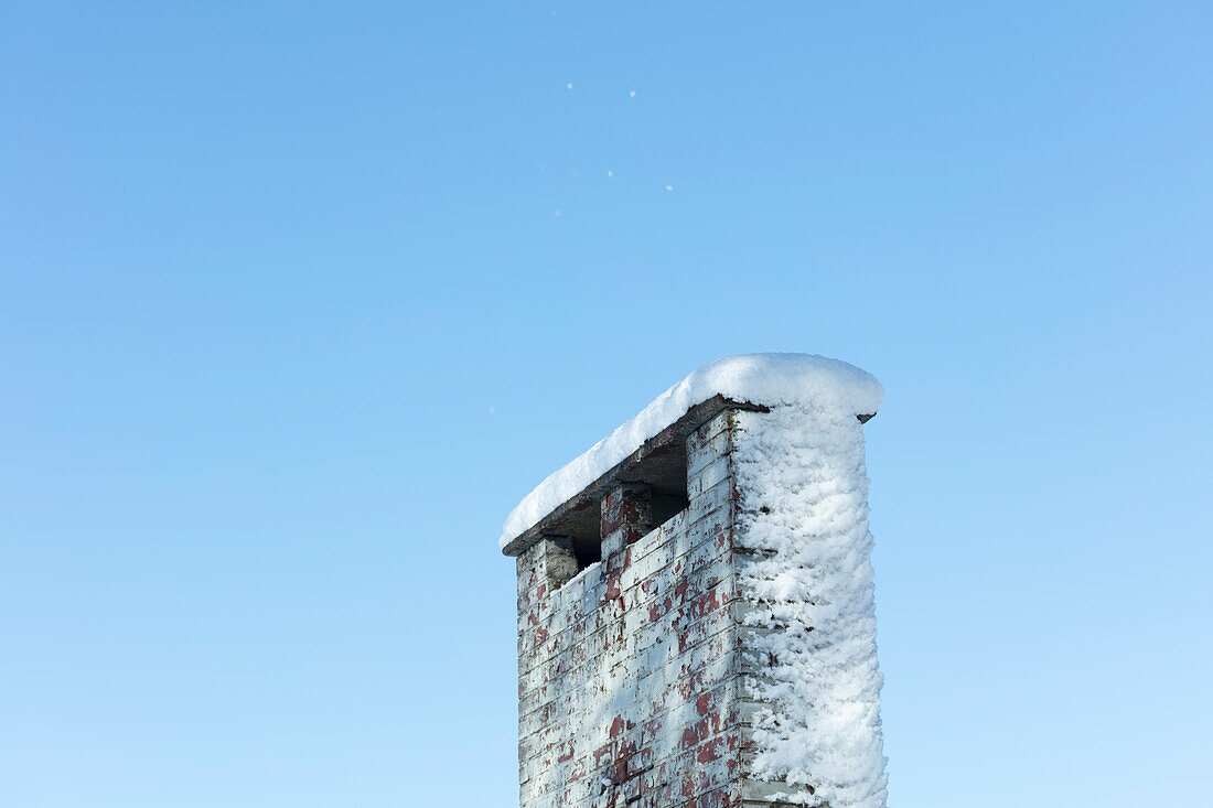 Snow on brick chimney against blue sky