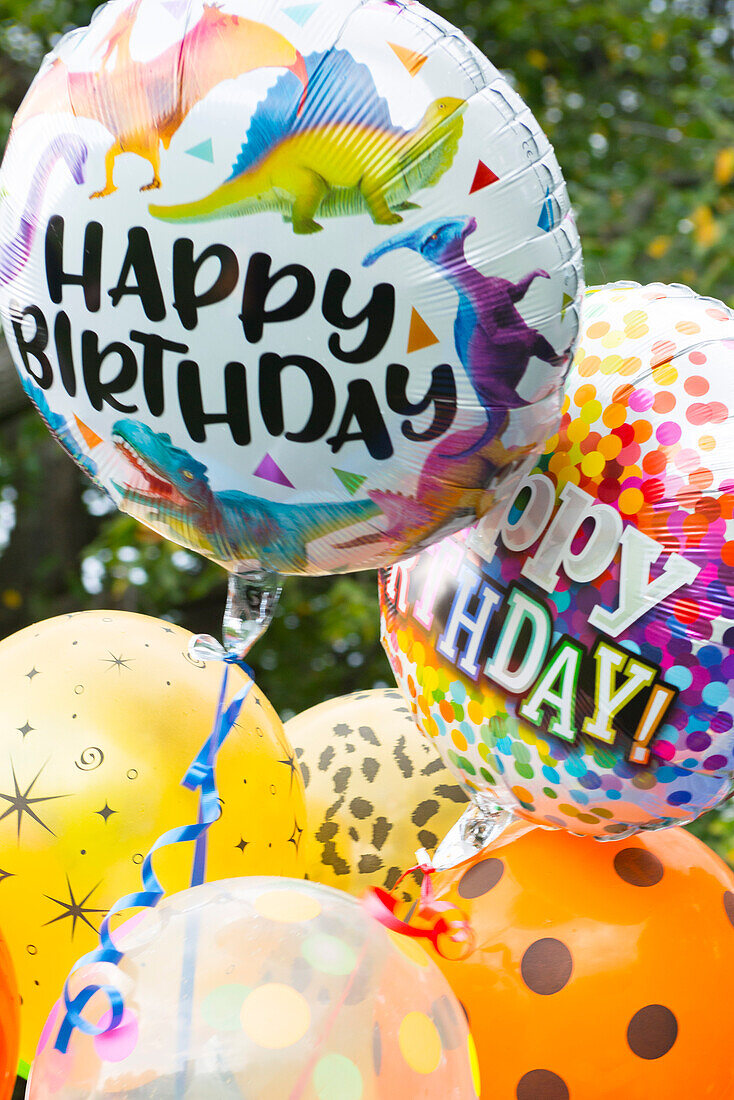 Several 'Happy Birthday" and colorful helium-filled balloons in an outdoor setting