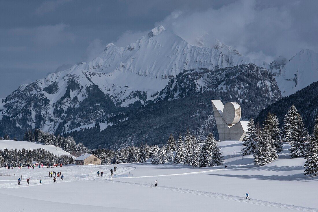 France, Haute Savoie, Bornes massif, Glieres plateau, skating skiers on cross country ski trails and the national monument of the resistance of Emile Gilioli and the peak of Jalouvre