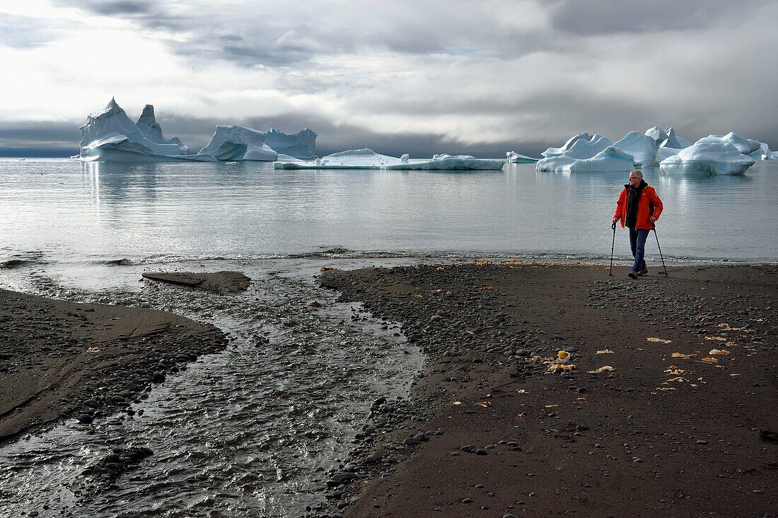 Greenland, west coast, Disko Island, Qeqertarsuaq, hiker on the beach and icebergs in the background