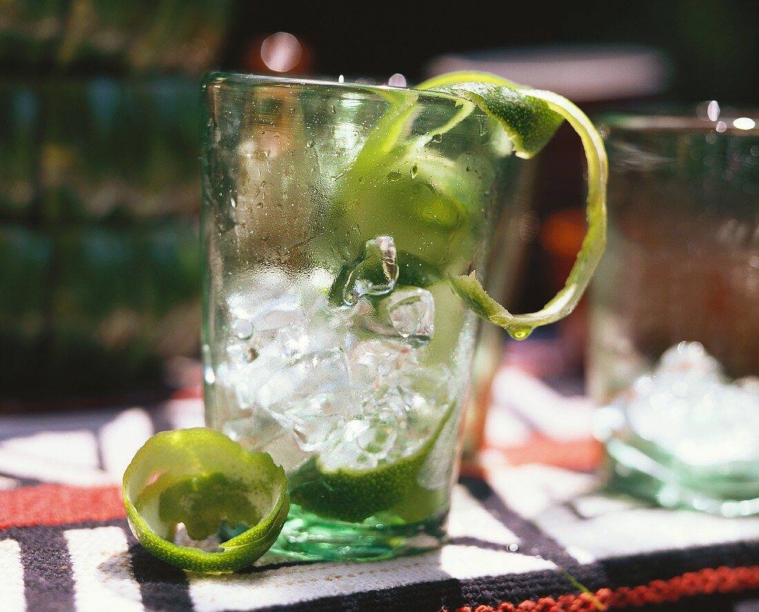 Tequila with ice cubes in glass, garnished with lime skin
