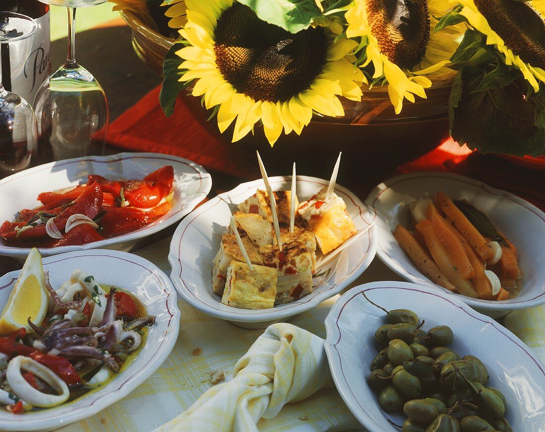 Spanische Tapas auf Platten auf Gartentisch mit Sonnenblumen