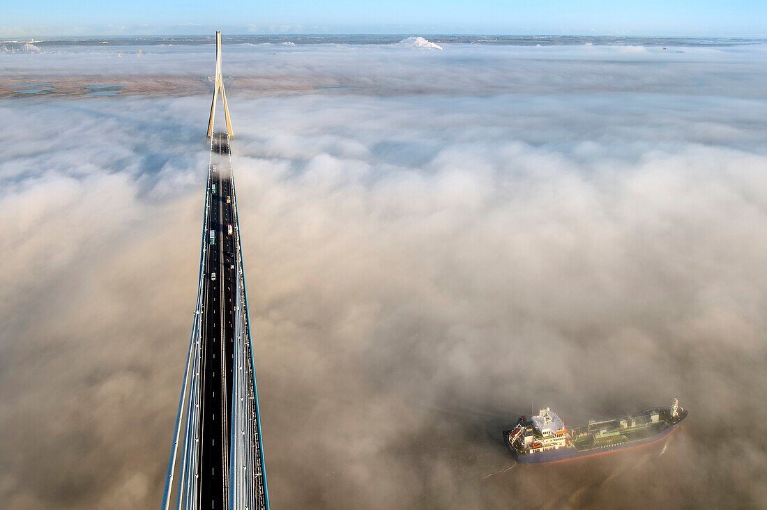 Frankreich, zwischen Calvados und Seine Maritime, Frachtgut fährt unter der Pont de Normandie (Normandie-Brücke) hindurch, die aus dem morgendlichen Herbstnebel auftaucht und die Seine überspannt, im Hintergrund das Naturschutzgebiet der Seine-Mündung, Blick von der Spitze des Südpylons