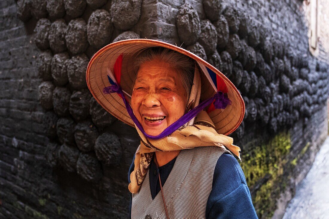 Vietnam, Hanoi province, Bat Trang, the village of ceramists, smiling woman in front of lumps of charcoal stuck on a wall of a traditional house