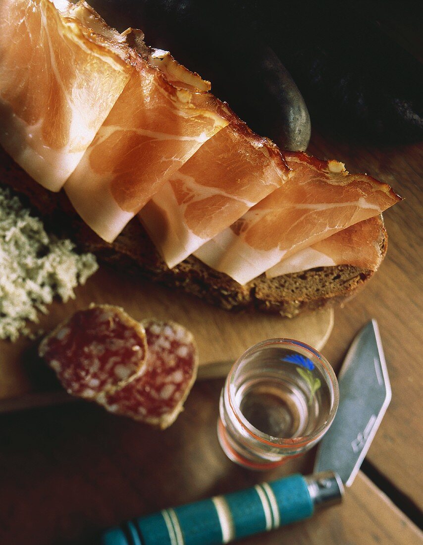 Brotzeit mit Schinkenbrot, Salami & Schnaps auf Holztisch