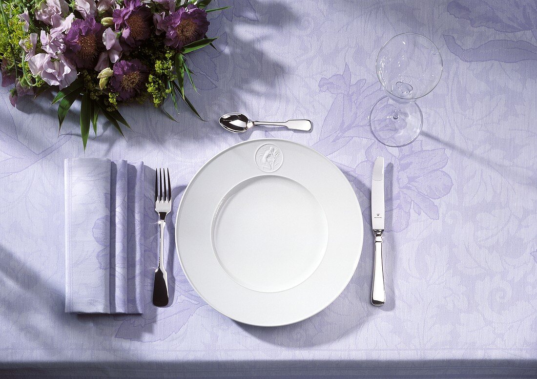 Ein Gedeck (Teller,Besteck,Weinglas) auf violettem Tischtuch