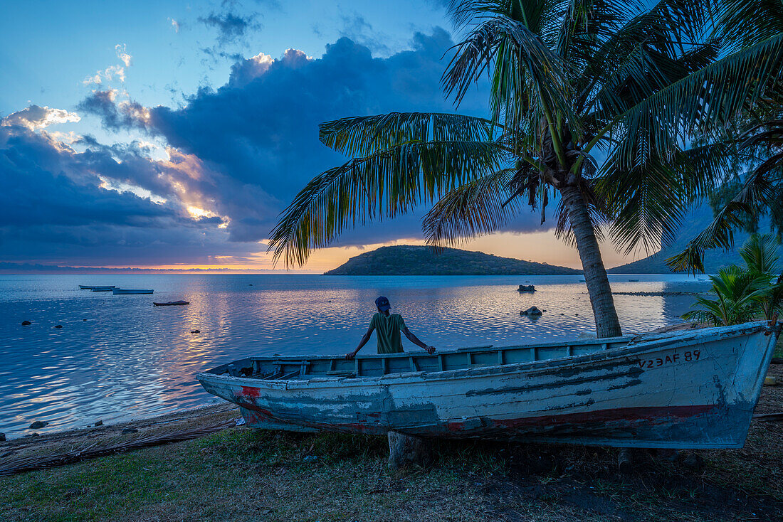 Blick auf einen Einheimischen, der auf einem Boot sitzt und Le Morne von Le Morne Brabant aus bei Sonnenuntergang betrachtet, Distrikt Savanne, Mauritius, Indischer Ozean, Afrika