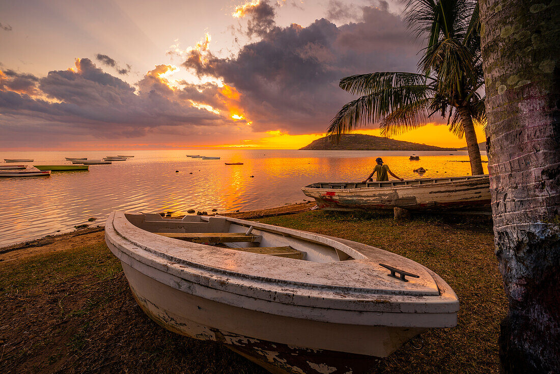 View of local man sat on boat viewing Le Morne from Le Morne Brabant at sunset, Savanne District, Mauritius, Indian Ocean, Africa