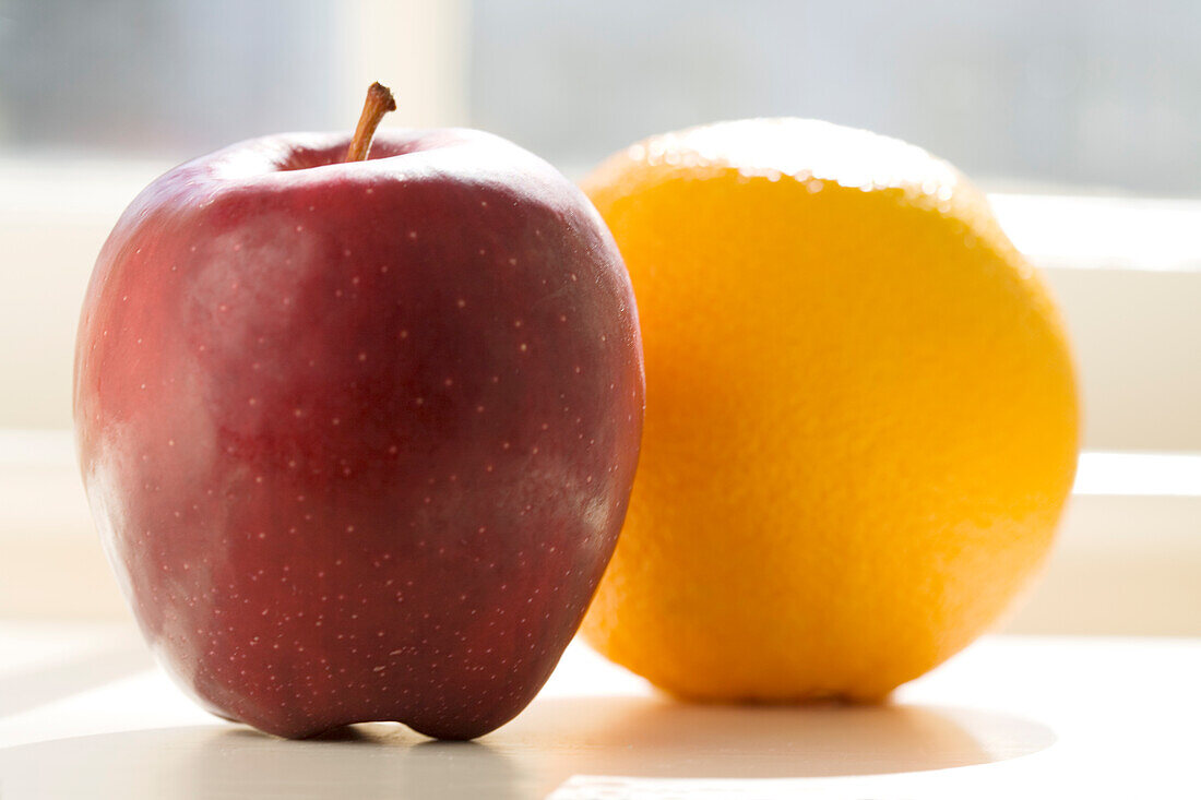 Apple and orange on table in sunlight