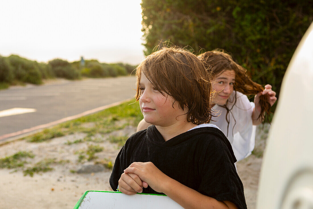 Südafrika, Hermanus, Porträt eines Jungen mit Surfbrett und Schwester am Strand