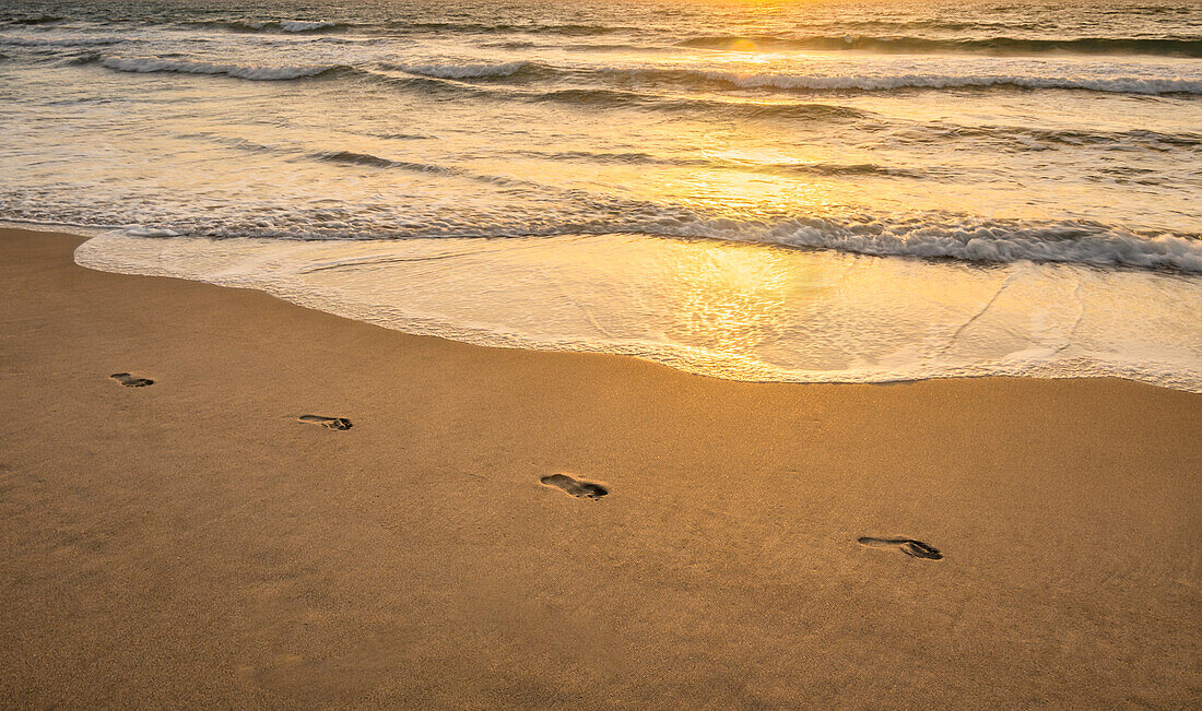 Footprints on sandy beach at sunset