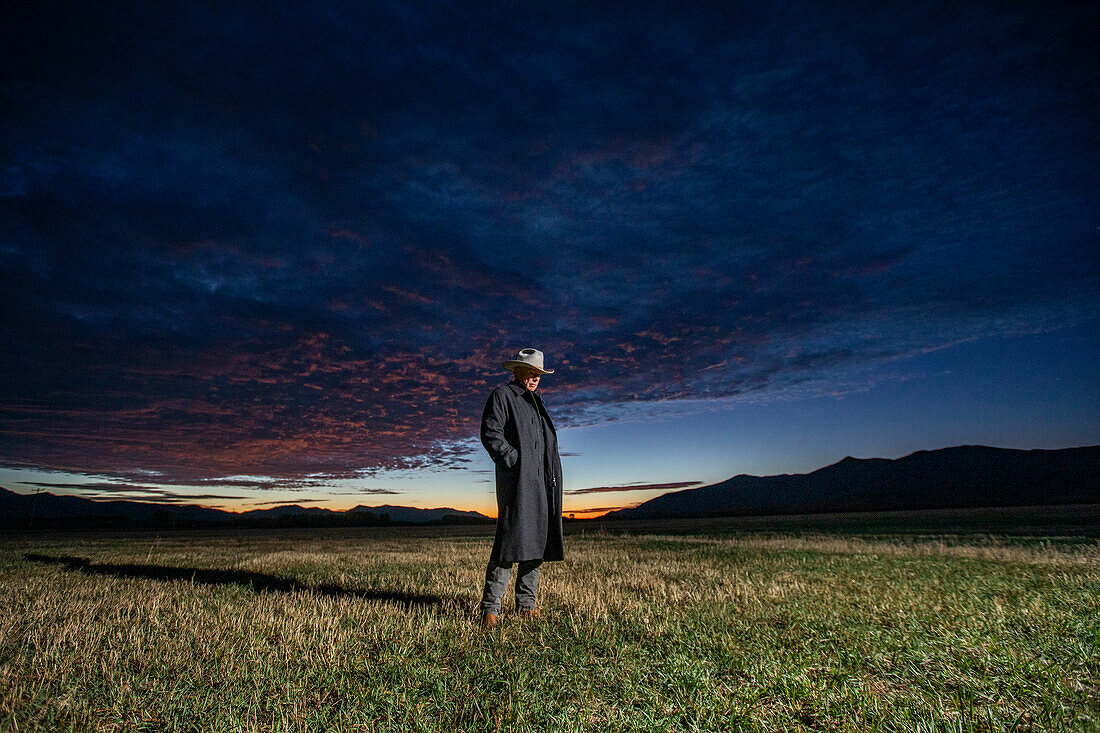 USA, Idaho, Bellevue, Rancher in overcoat standing in field at sunrise