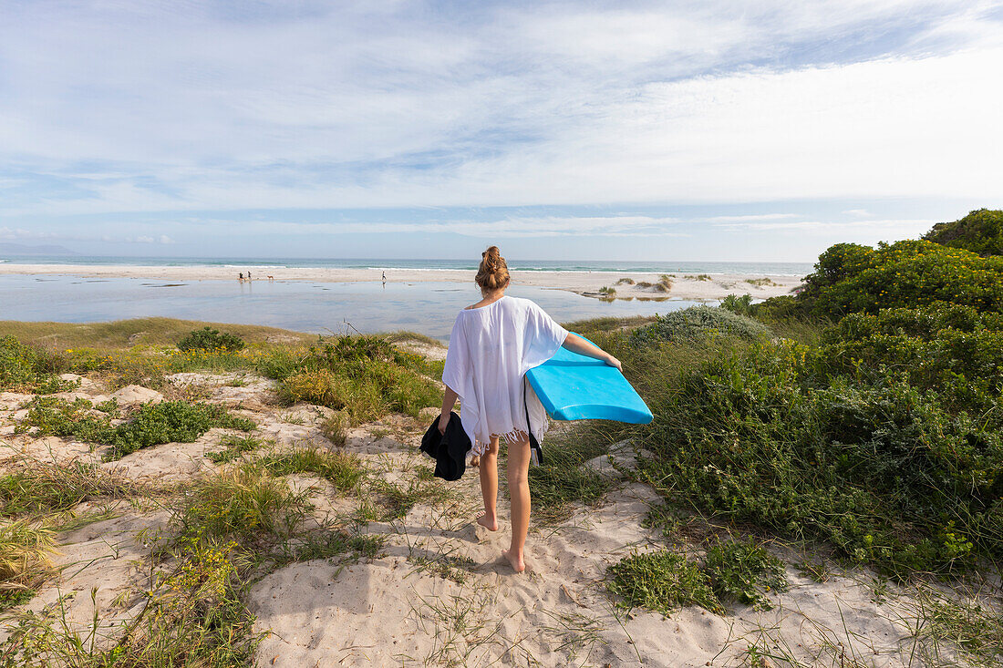 Südafrika, Hermanus, Teenager-Mädchen geht am Strand mit Bodyboard spazieren