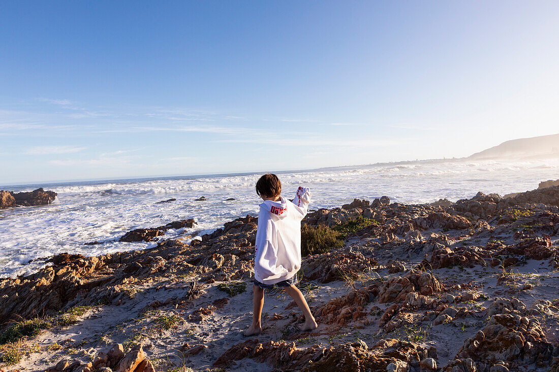 South Africa, Hermanus, Boy (10-11) walking on rocks on Kammabaai Beach