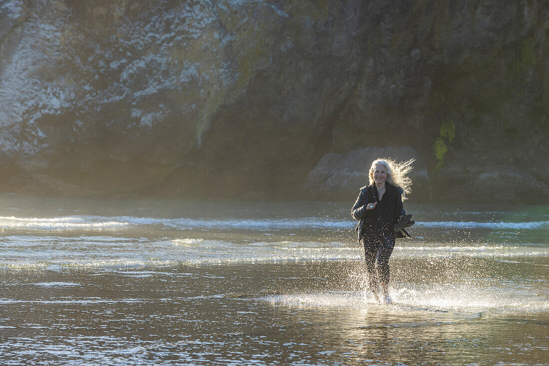 USA, Oregon, Newport, Frau läuft am Sandstrand und spritzt Wasser