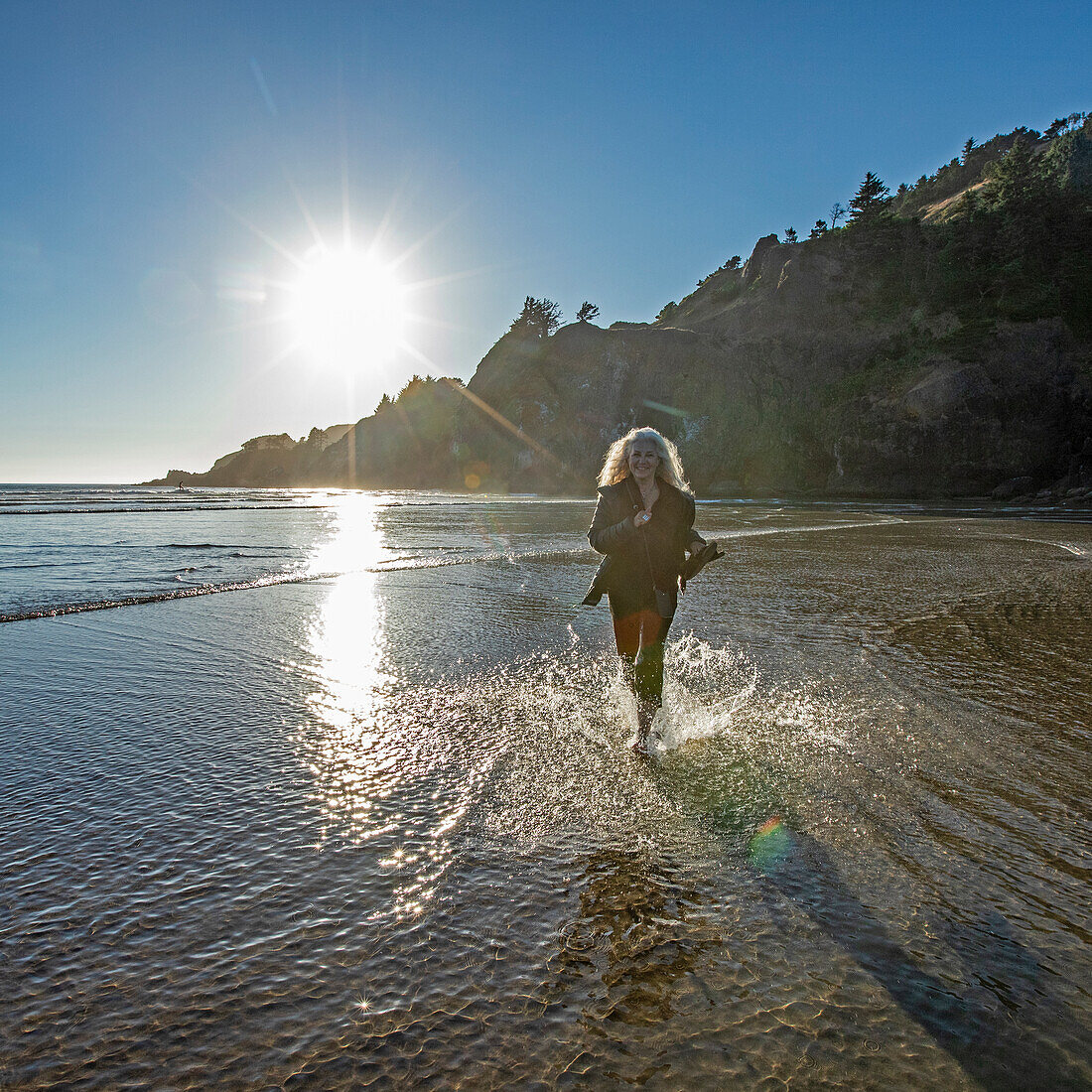 USA, Oregon, Newport, Frau läuft am Sandstrand und spritzt Wasser