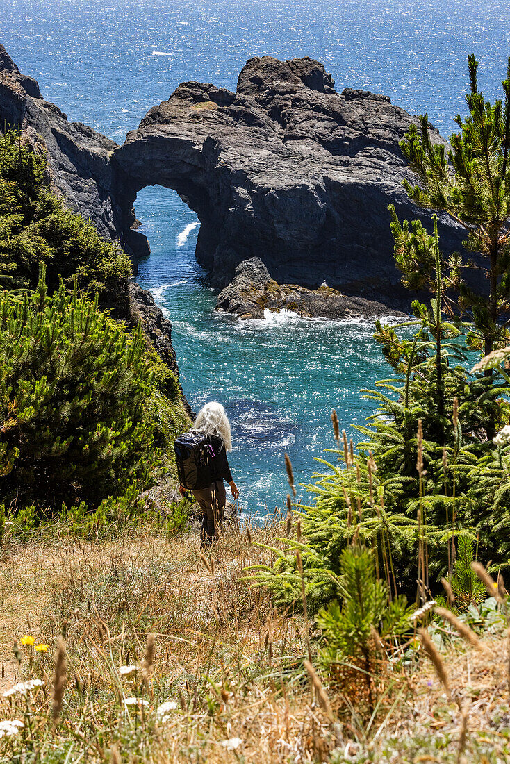 USA, Oregon, Brookings, Ältere Frau beim Wandern zwischen Felsen über dem Meer