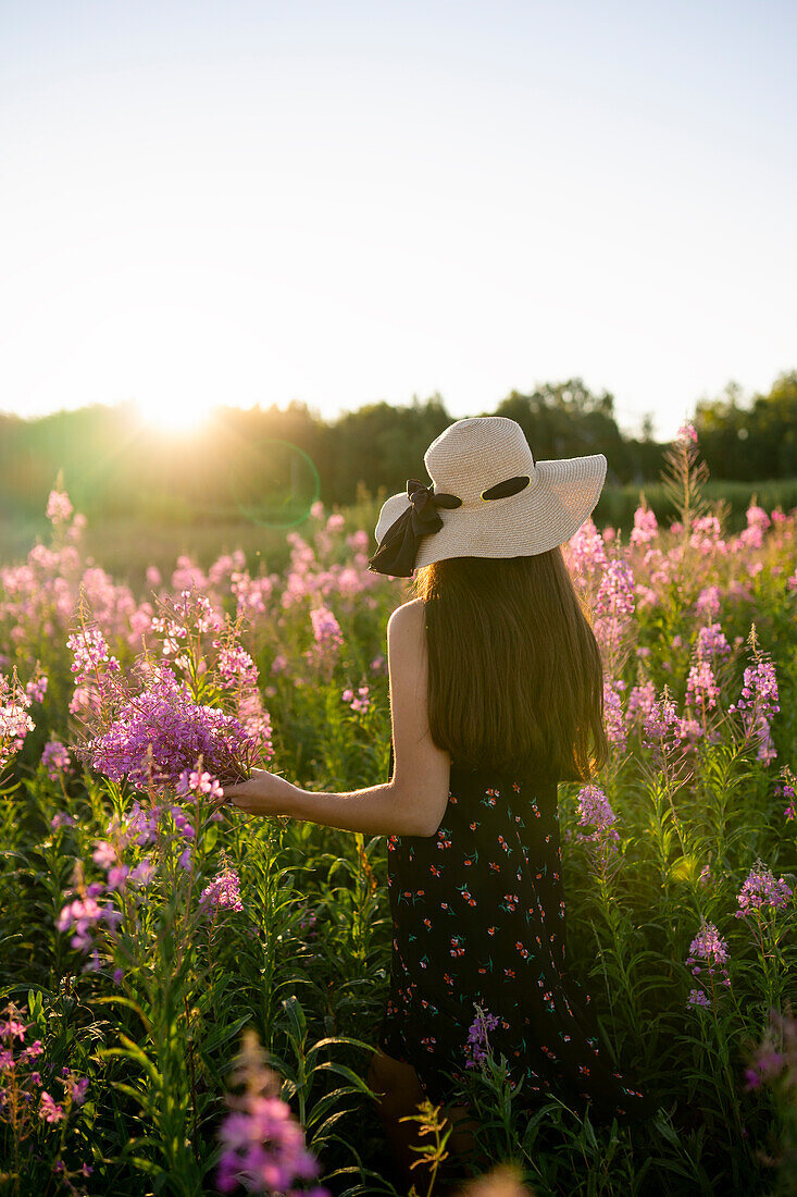 Rear view of woman in straw hat standing in meadow at sunset