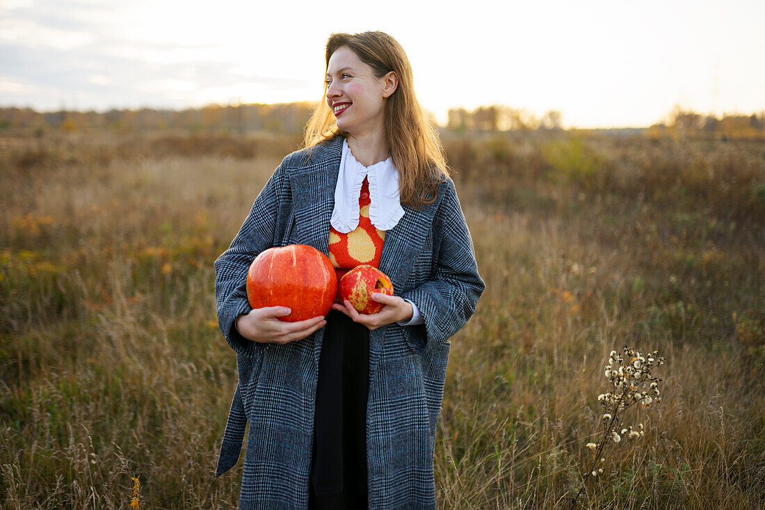 Portrait of smiling woman holding pumpkins in field