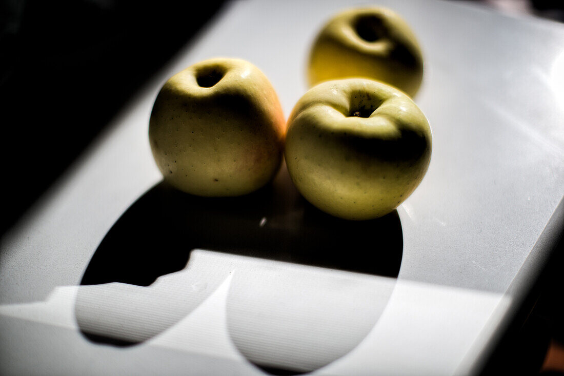 Three Apples Casting Shadows on a Reflective Surface