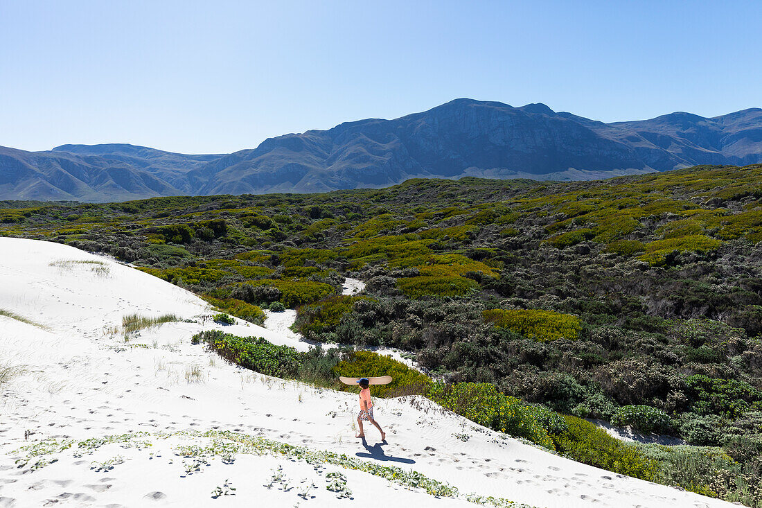 Südafrika, Junge (10-11) trägt Surfbrett im Walker Bay Naturreservat