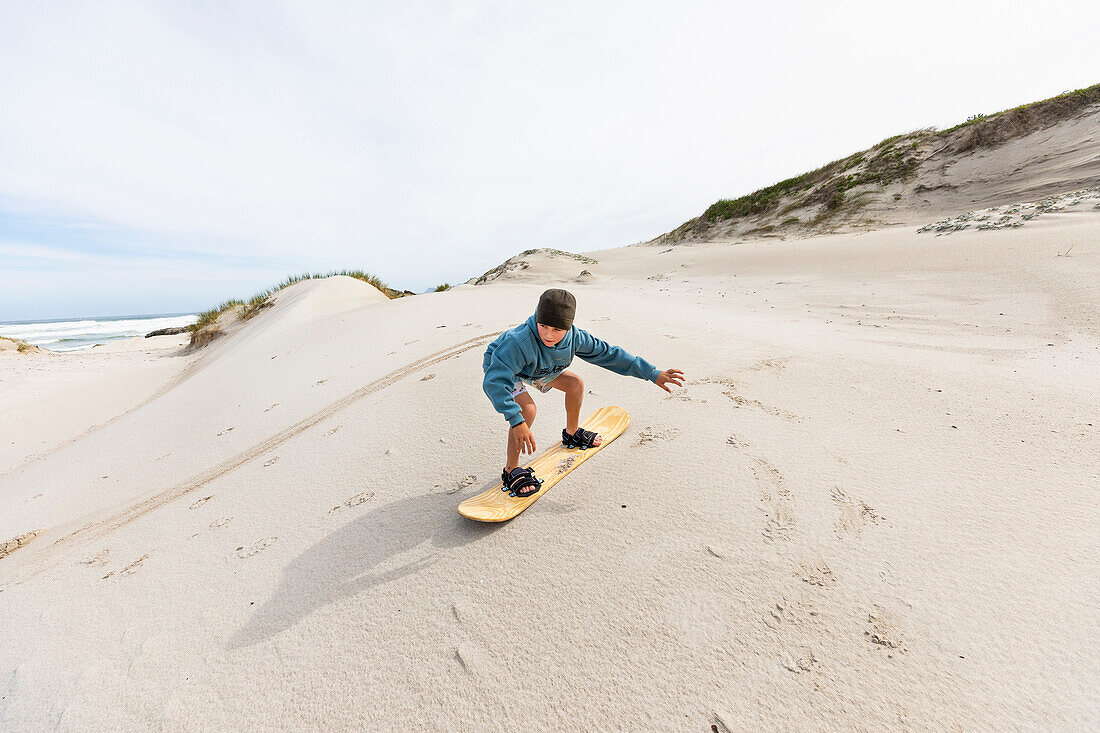 Junge (10-11) beim Sandboarden im Walker Bay Naturreservat