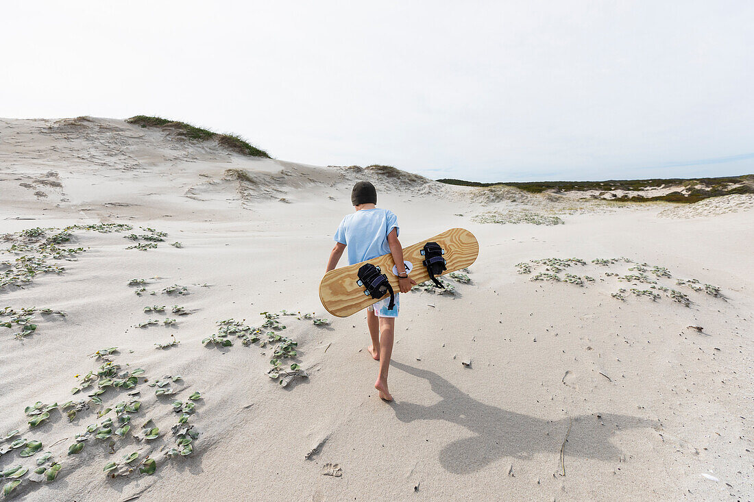 Junge (10-11) trägt Surfbrett im Walker Bay Naturreservat