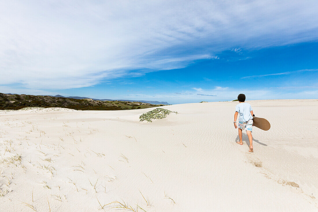 Junge (10-11) trägt Surfbrett im Walker Bay Naturreservat