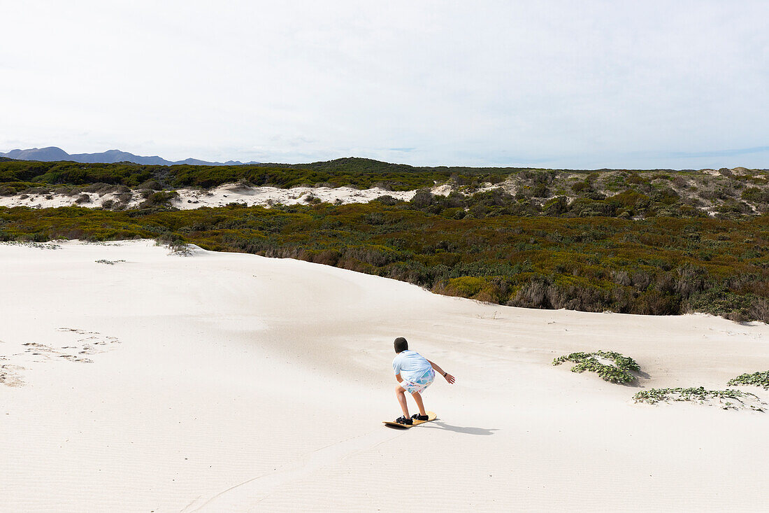 Junge (10-11) beim Sandboarden im Walker Bay Naturreservat