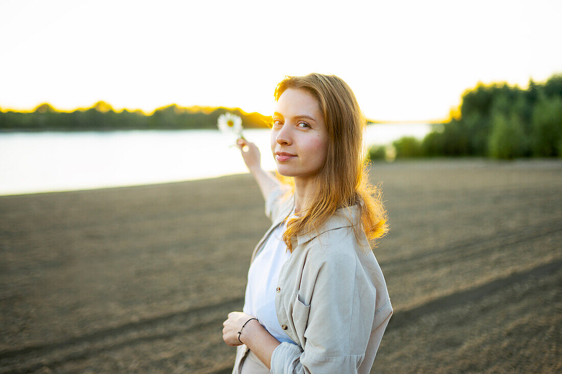 Porträt einer Frau mit einer Blume am Strand bei Sonnenuntergang