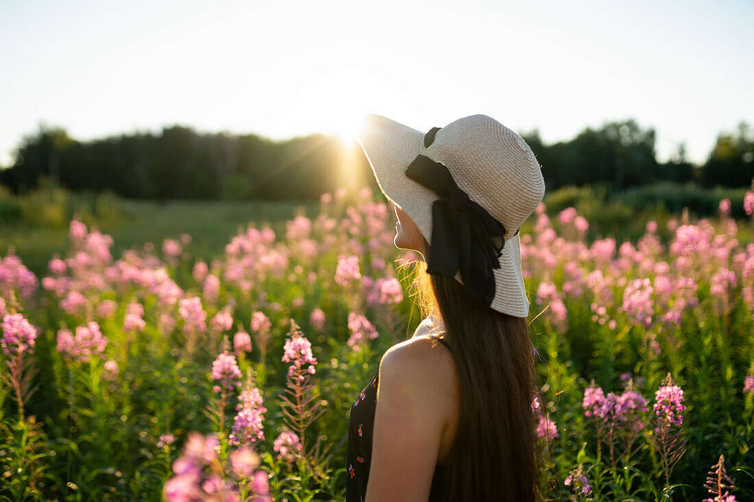 Junge Frau mit Strohhut, die an einem sonnigen Tag auf einer Wiese steht