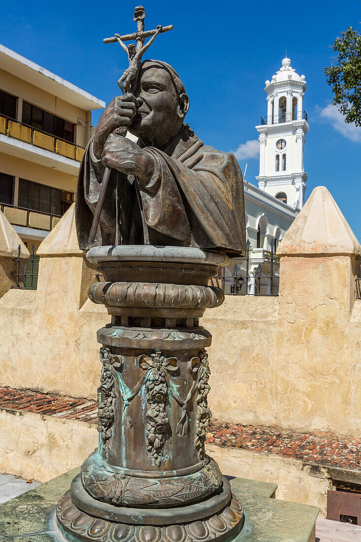Bust of Pope John Paul II, Cathedral of Santo Domingo, Cathedral of Santa Maria La Menor, Santo Domingo, Dominican Republic. It was the first cathedral built in the Americas, completed about 1540 A.D. & is a Minor Basilica. UNESCO World Heritage Site of the Colonial City of Santo Domingo. In the background is the white clock tower of the first city hall built in the Americas.