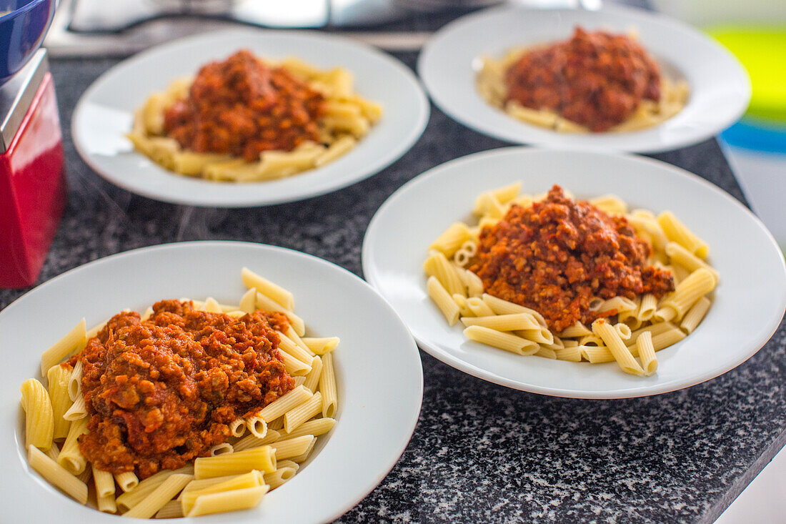 Makkaroni mit Bolognesesoße, serviert auf vier Tellern