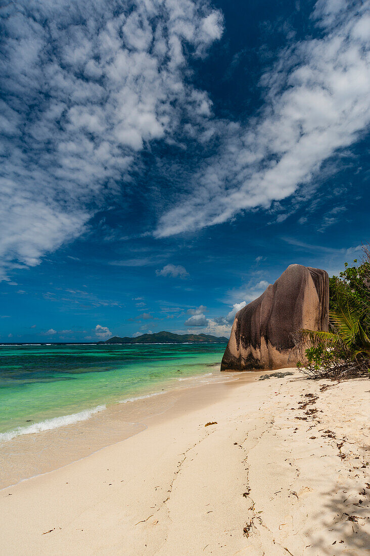 Wispy Clouds über einem tropischen Sandstrand mit einer großen Felsformation. Strand Anse Source d 'Argent, Insel La Digue, Seychellen.