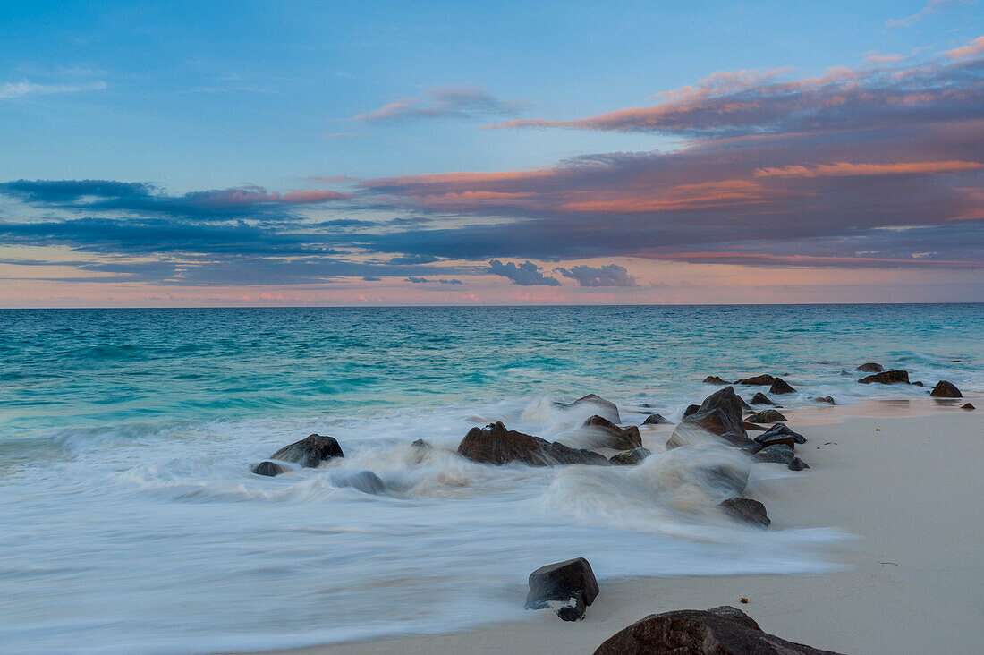 Langzeitbelichtung der Brandung des Indischen Ozeans, die bei Sonnenuntergang auf einen felsigen Strand trifft. Anse Bambous Strand, Fregate Insel, Seychellen.