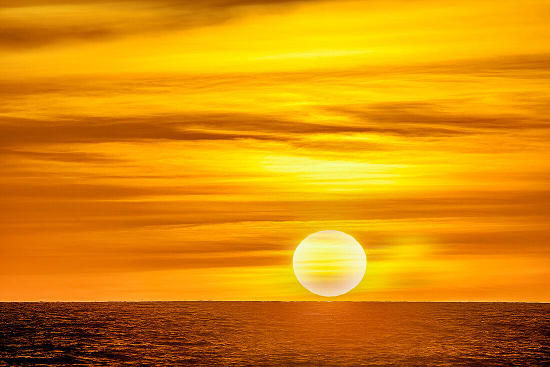 Das goldene Licht der wirbelnden Wolken bei Sonnenuntergang spiegelt sich in einem rosafarbenen Schimmer am Strand von Pererenan Beach, Bali, Indonesien