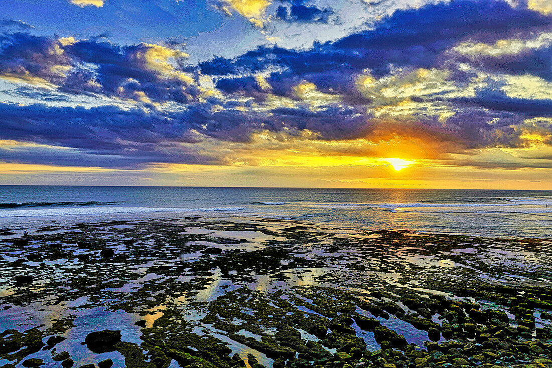 Das goldene Licht der untergehenden Sonne reflektiert einen goldenen Schimmer auf dem Strand von Pererenan Beach, während die Wellen auf Bali, Indonesien, anrollen