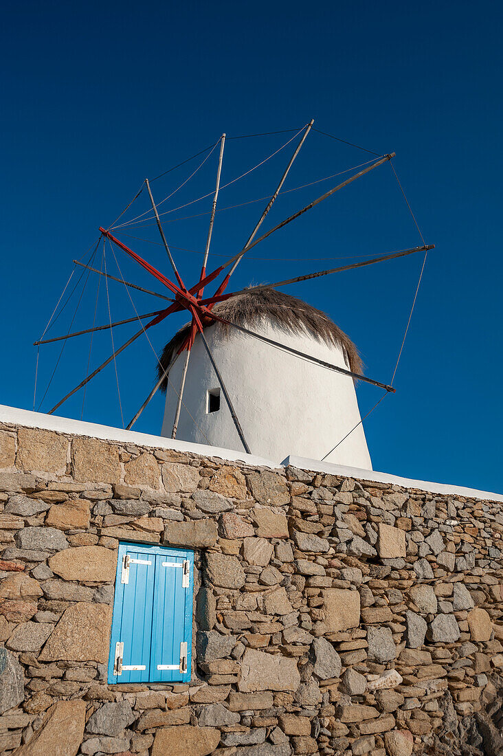 A traditional windmill set behind a rock masonry wall. Chora, Mykonos Island, Cyclades Islands, Greece.