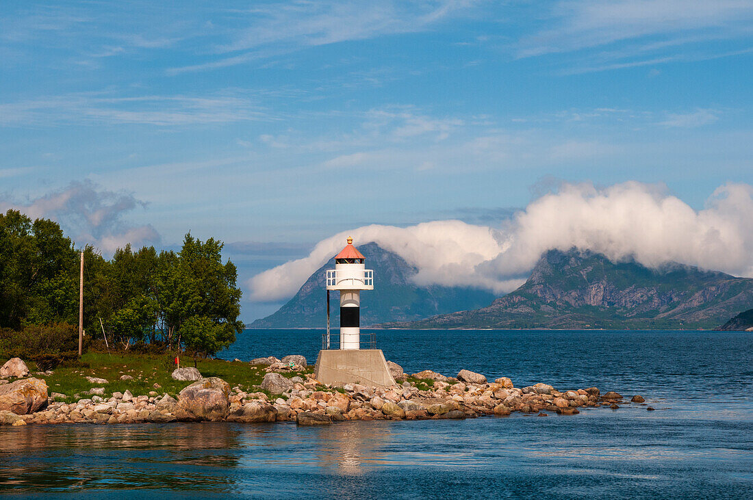 Ein Leuchtturm thront auf einem Felsvorsprung und spiegelt den Holandsfjord. Svartisen, Norwegen.