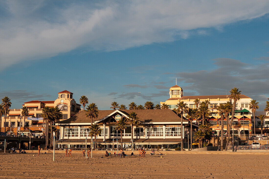 Volleyballspieler am Huntington Beach vor den sonnenbeschienenen Gebäuden am Wasser. Huntington Beach, Kalifornien, USA. (Nur für redaktionelle Zwecke)