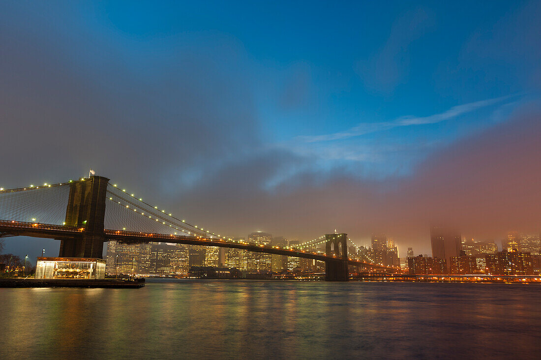 Die Skyline von Manhattan und die Brooklyn Bridge im Dunst der Abenddämmerung.