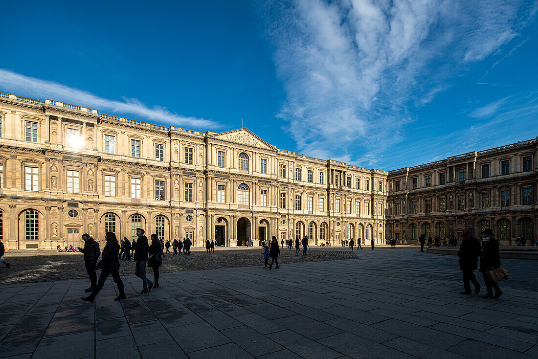 Visitors strolling through the Cour Carrées North Wing at the Louvre on a clear day.